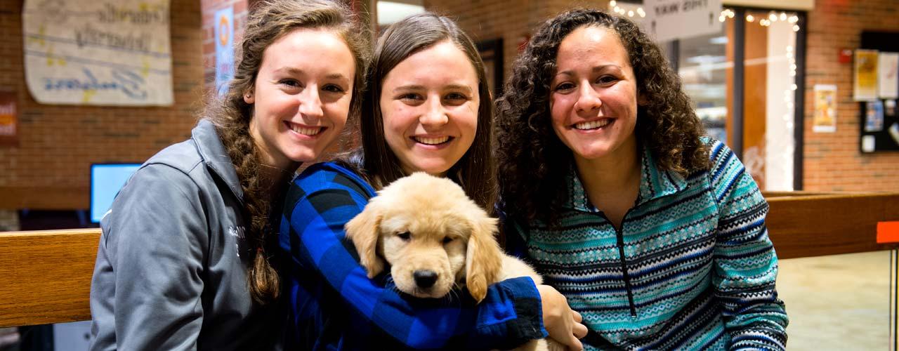 Three female students cuddle with a puppy in the lower Stevens Student Center